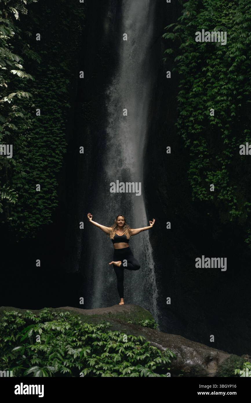 Woman in yoga tree pose with arms extended of a jungle waterfall Stock ...