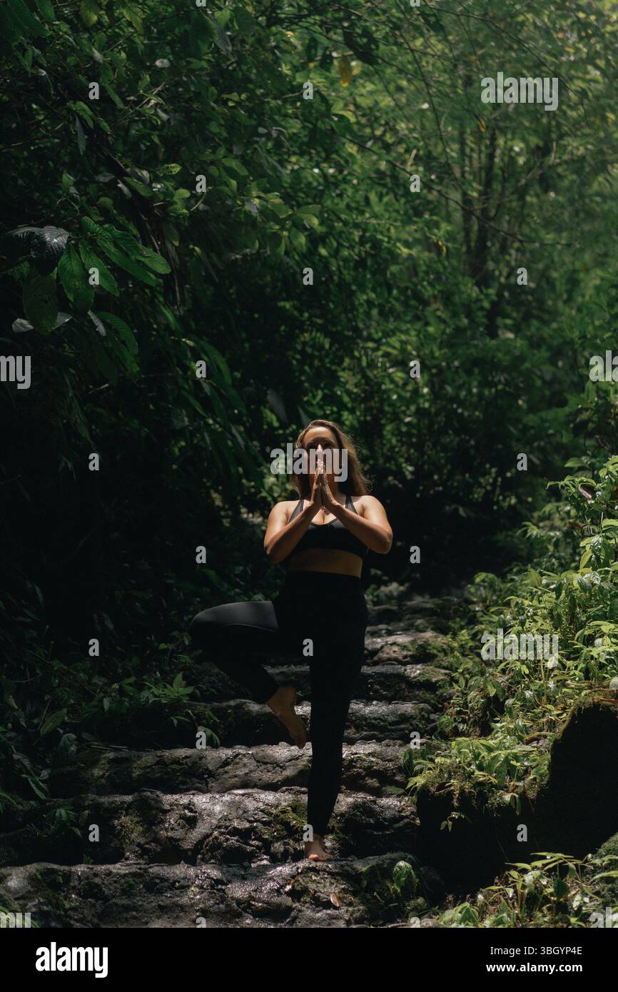 Woman practicing yoga pose in forest surrounded by lush greenery Stock Photo