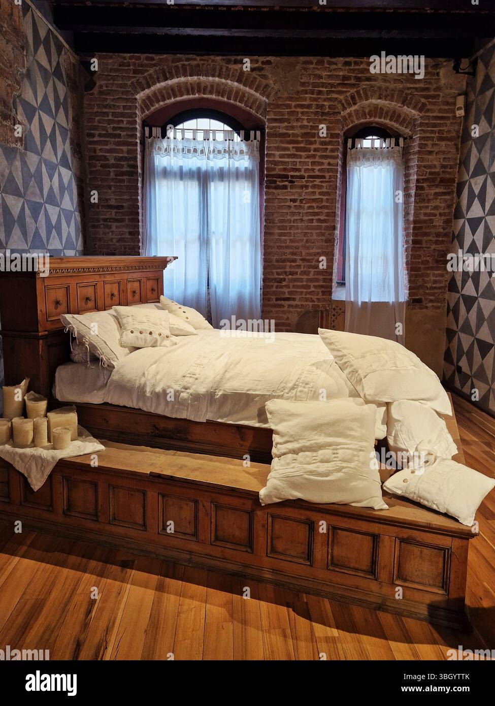 Rustic Bedroom With Exposed Brick and Wooden Furniture in Warm Lighting. Verona, Italy Stock Photo