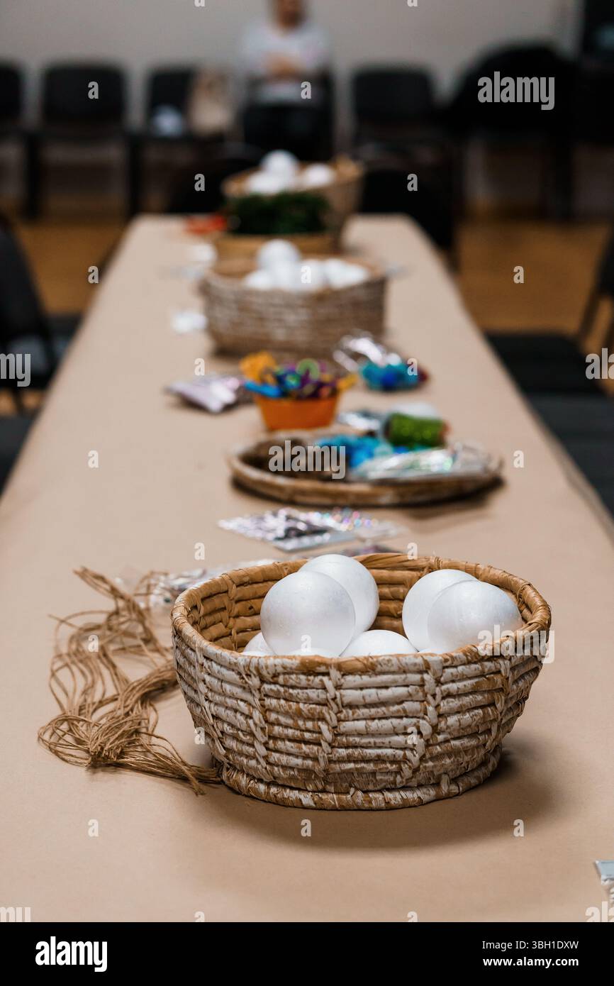 A long table is arranged for a creative workshop, displaying baskets filled with art supplies like colored eggs, twine, and craft materials, ready for Stock Photo