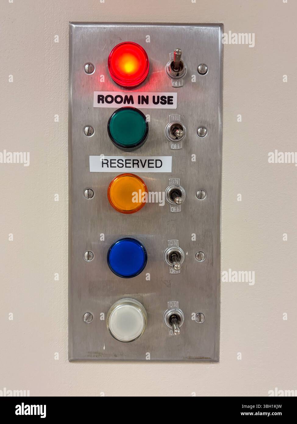A wall-mounted metal panel features five colored lights with toggle switches, indicating room status Stock Photo