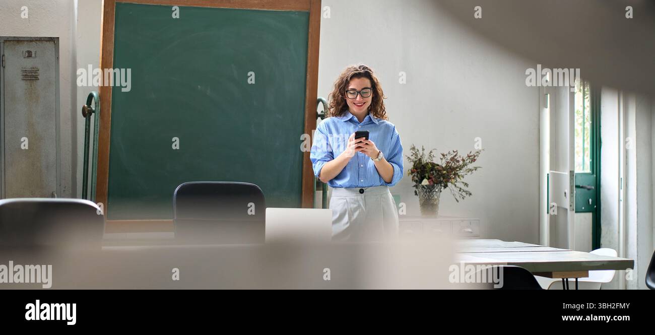 Smiling young business woman using cellphone standing in office using mobile. Stock Photo