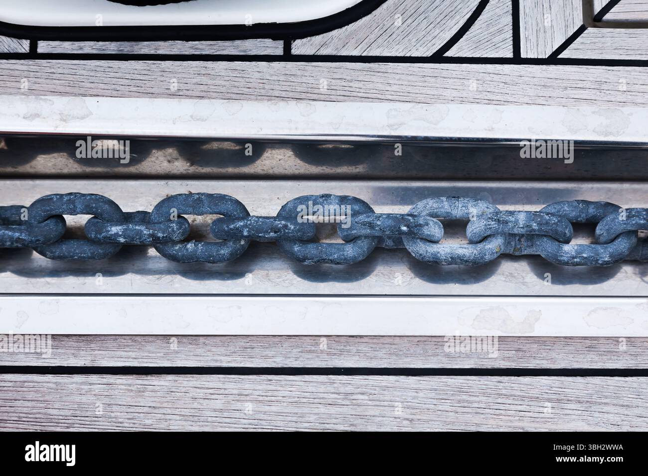 Anchor chain in a stainless steel niche, on the teak deck of a yacht, close-up. Stock Photo
