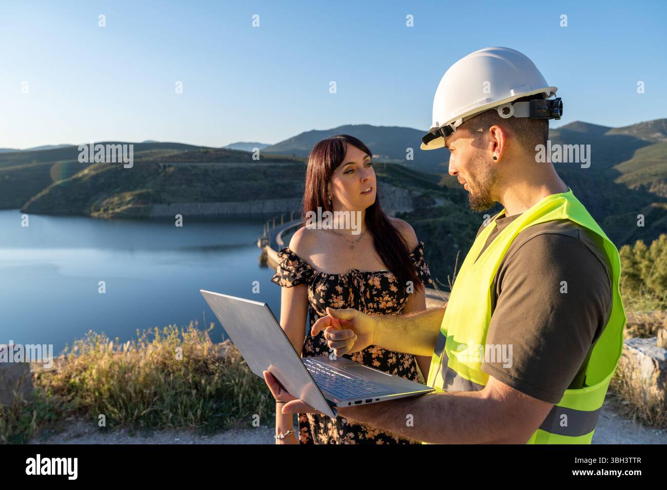 Engineers discussing a project using a laptop near a dam Stock Photo