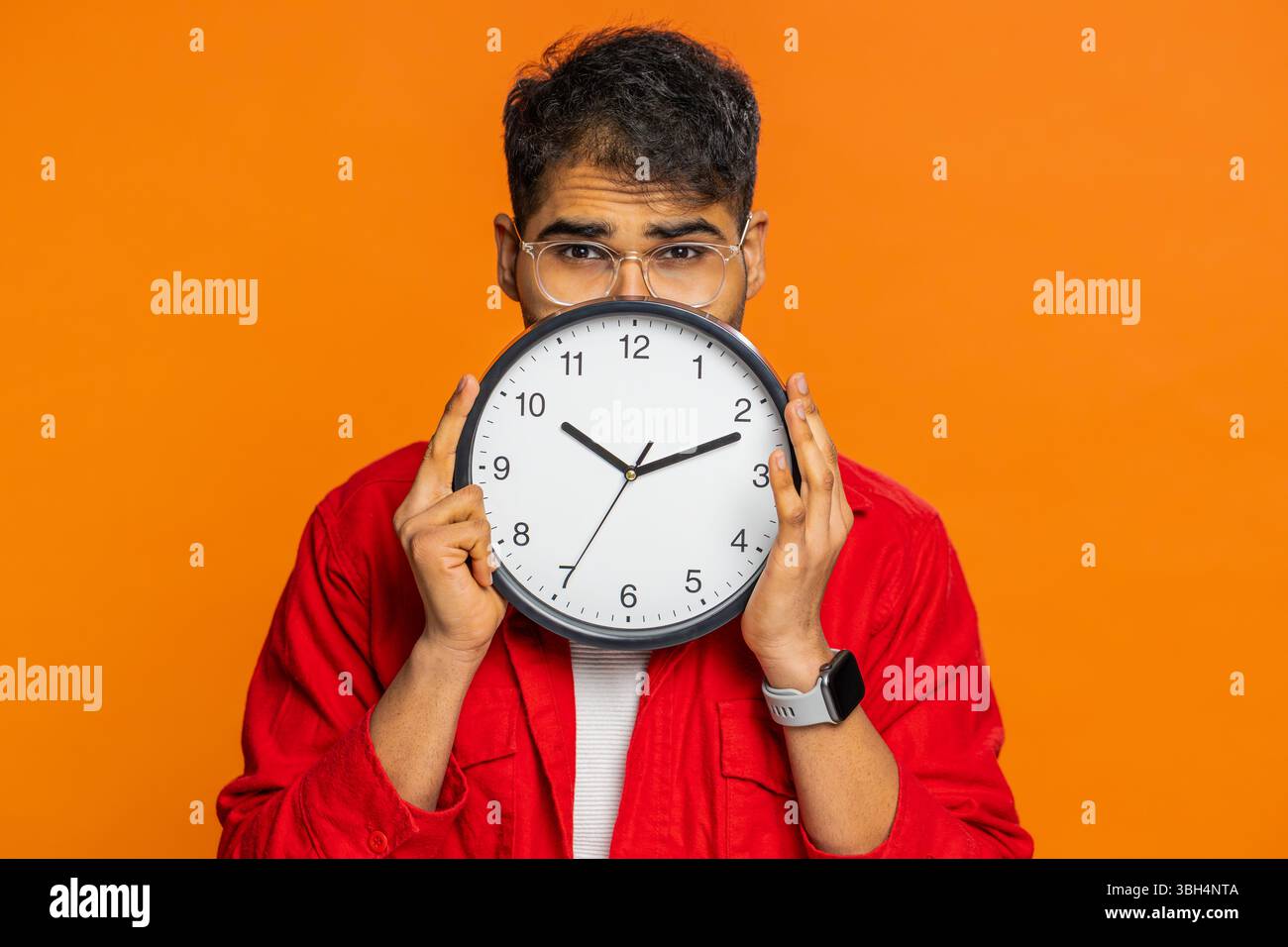 Serious strict Indian man holding office clock hiding behind, checking ...