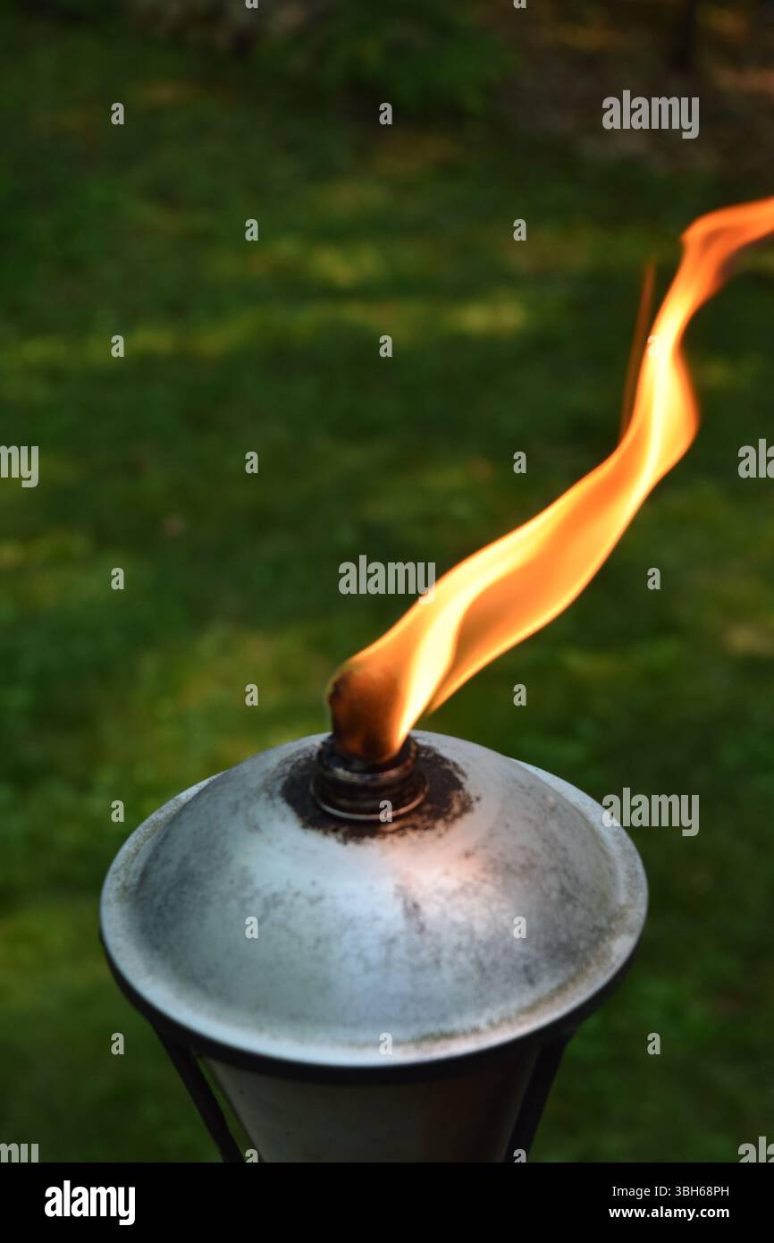 A close-up of a tiki torch flame flickering in the twilight, casting a ...
