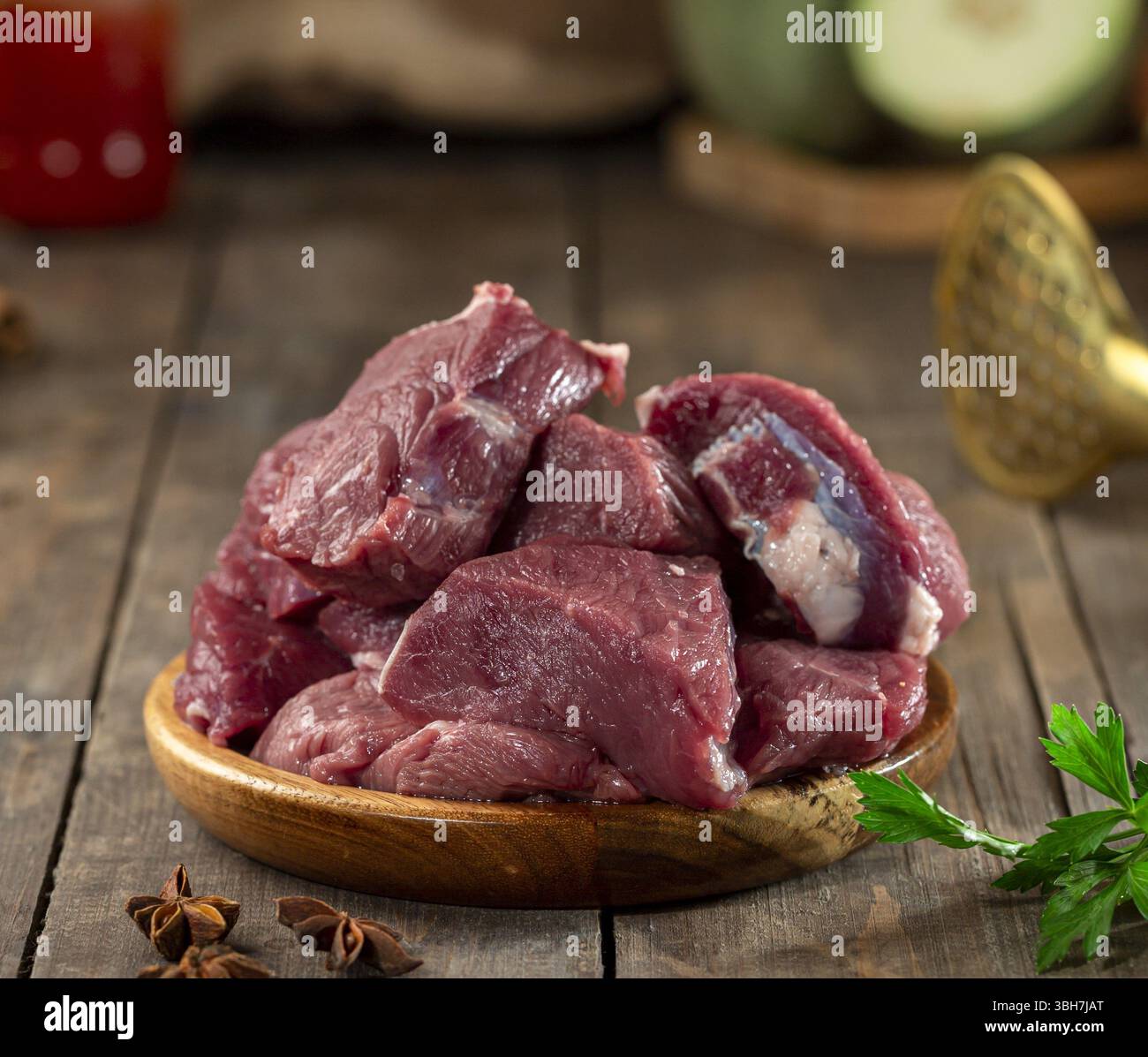 Raw veal chunks in wooden bowl on wooden surface. Stock Photo