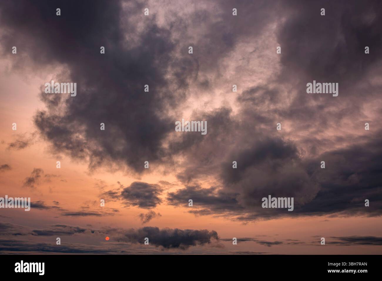 Cloudy sunset background backdrop with the orange sun breaking through the clouds. Stock Photo