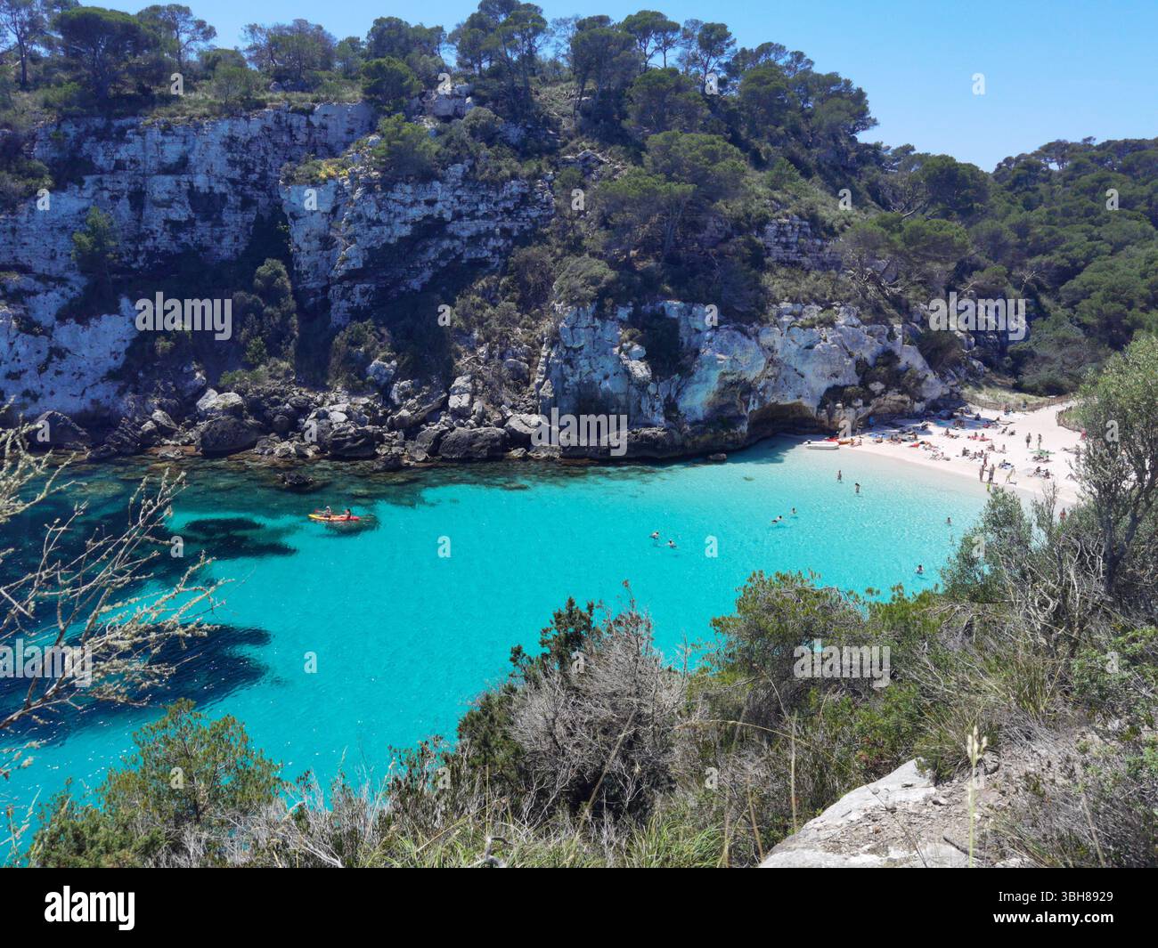 Turquoise beach, white sand, Mediterranean cliffs — Cala Macarelleta in Menorca, Spain, viewed from above with vibrant waters, pine forest and people - Smartphone Captured Stock Image