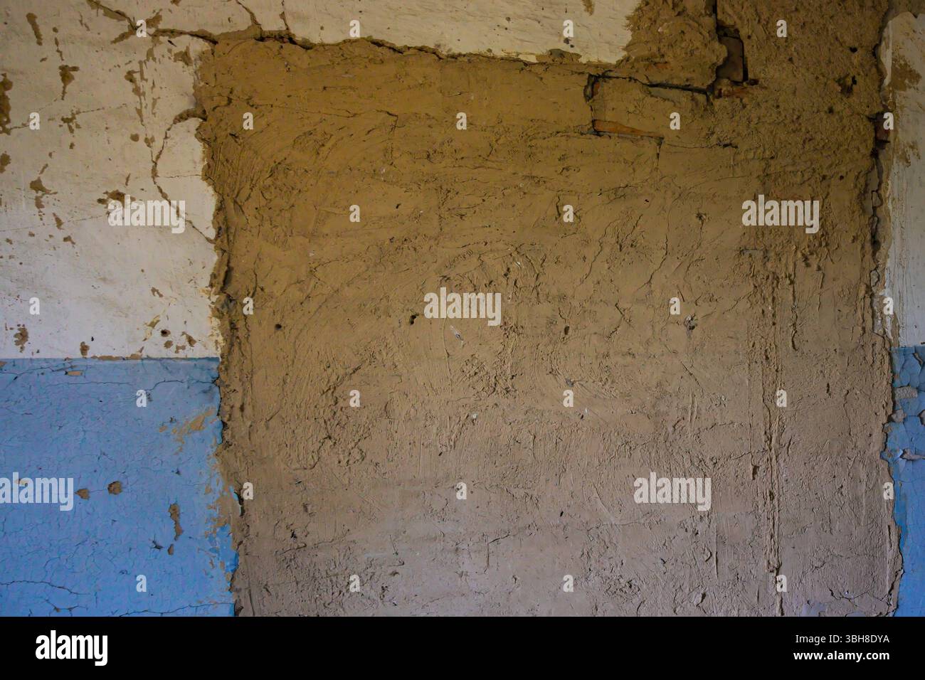 Peeling blue and beige plaster on a damaged wall. Cracks, old paint, and rough texture create an urban decay background for renovation, design, or gru Stock Photo