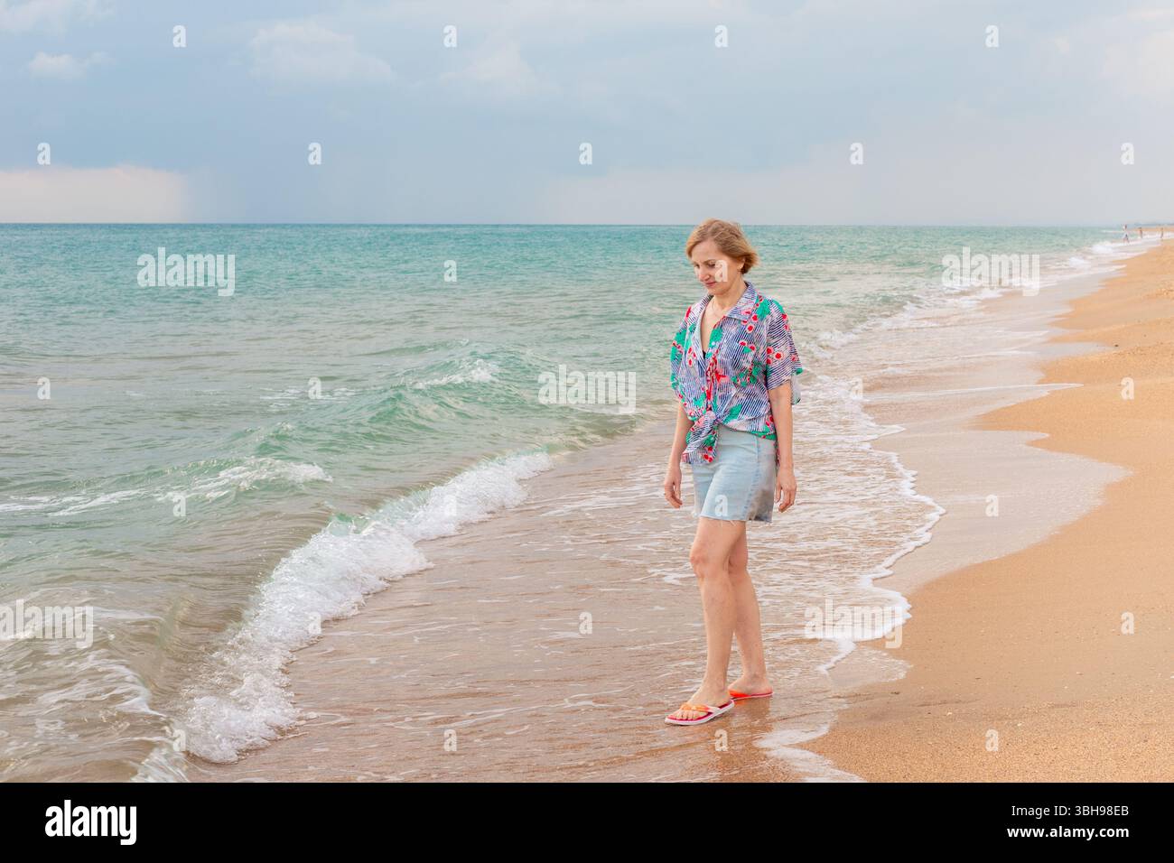 woman-in-floral-top-denim-shorts-and-sandals-walking-on-the-beach