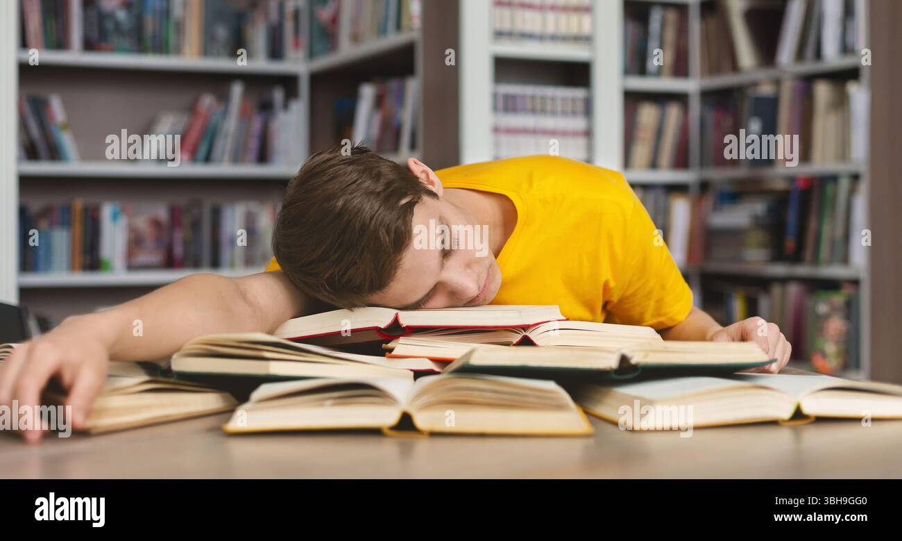 Tired guy napping on books in library Stock Photo
