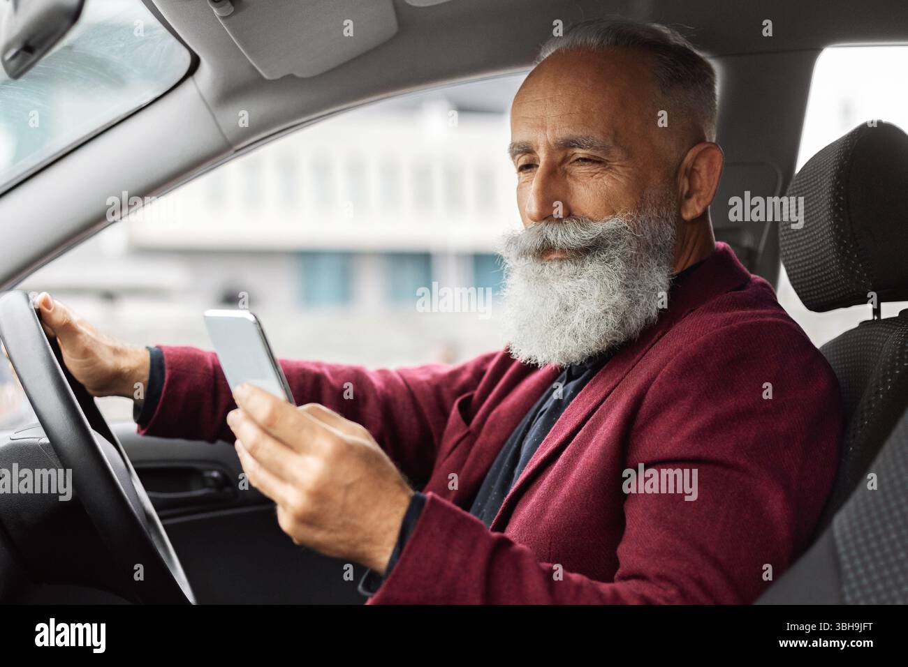 Elderly man driving new car, using mobile phone Stock Photo