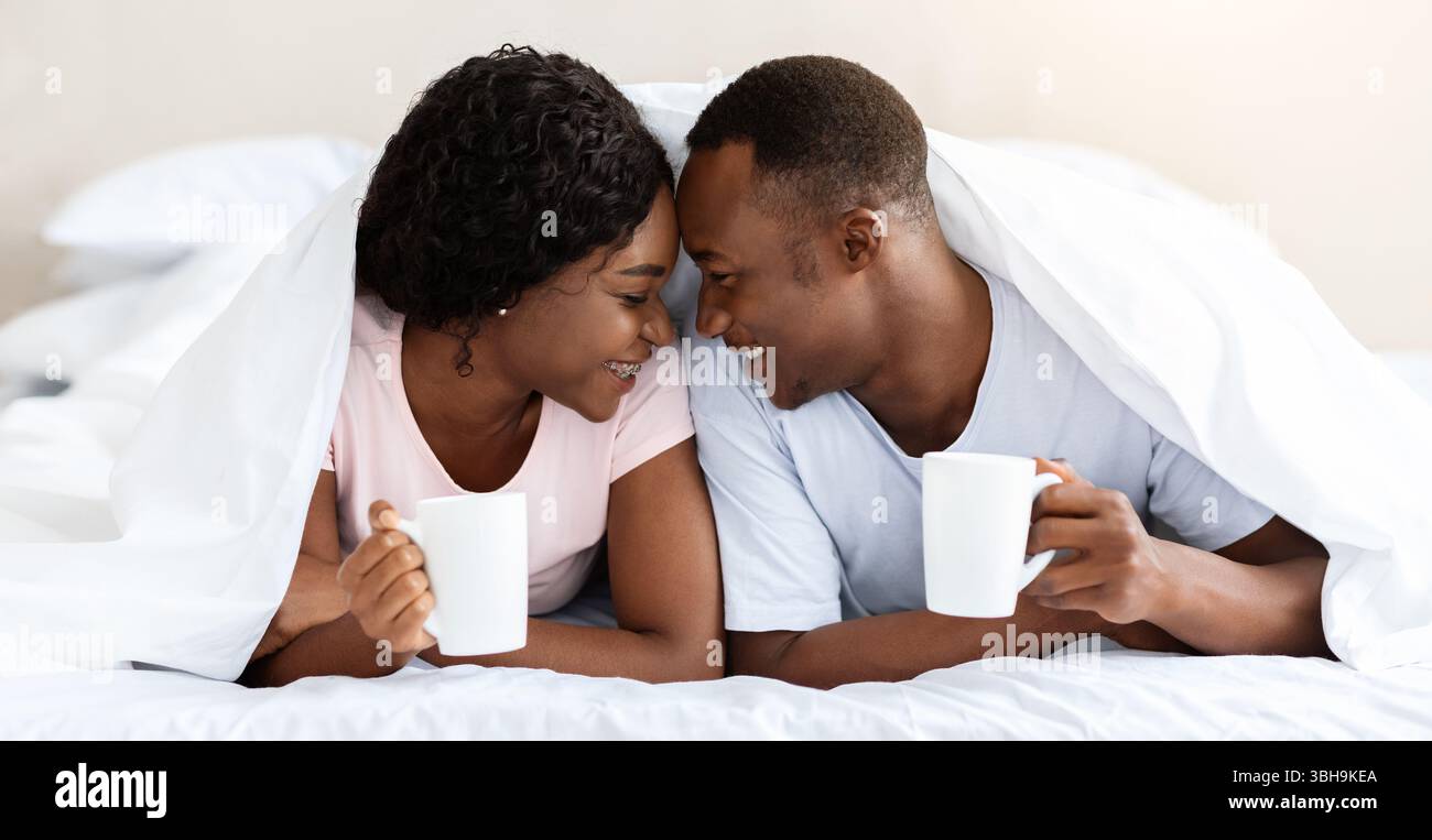 Romantic black couple laying under blanket, drinking tea Stock Photo