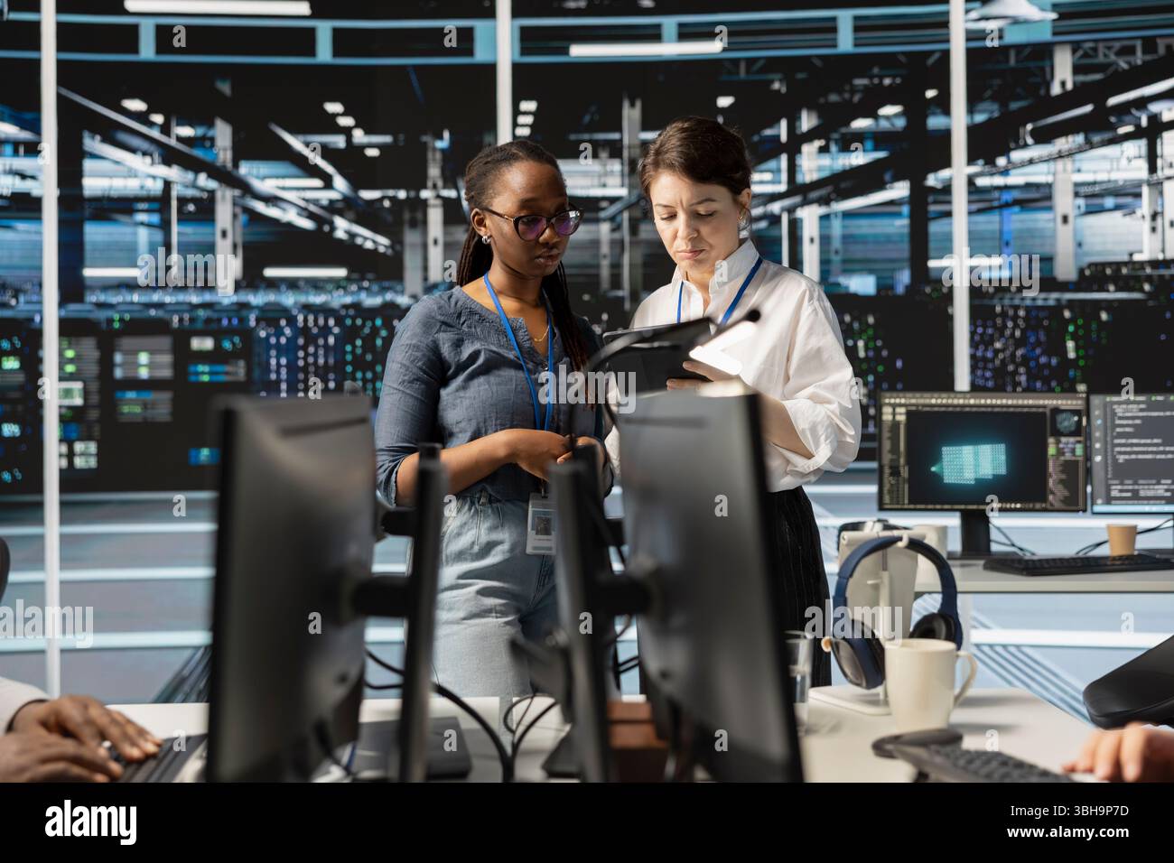 Team of technicians using tablet in server farm, analyzing data. Women working in data center examining infrastructure using device, ensuring system integrity and security Stock Photo