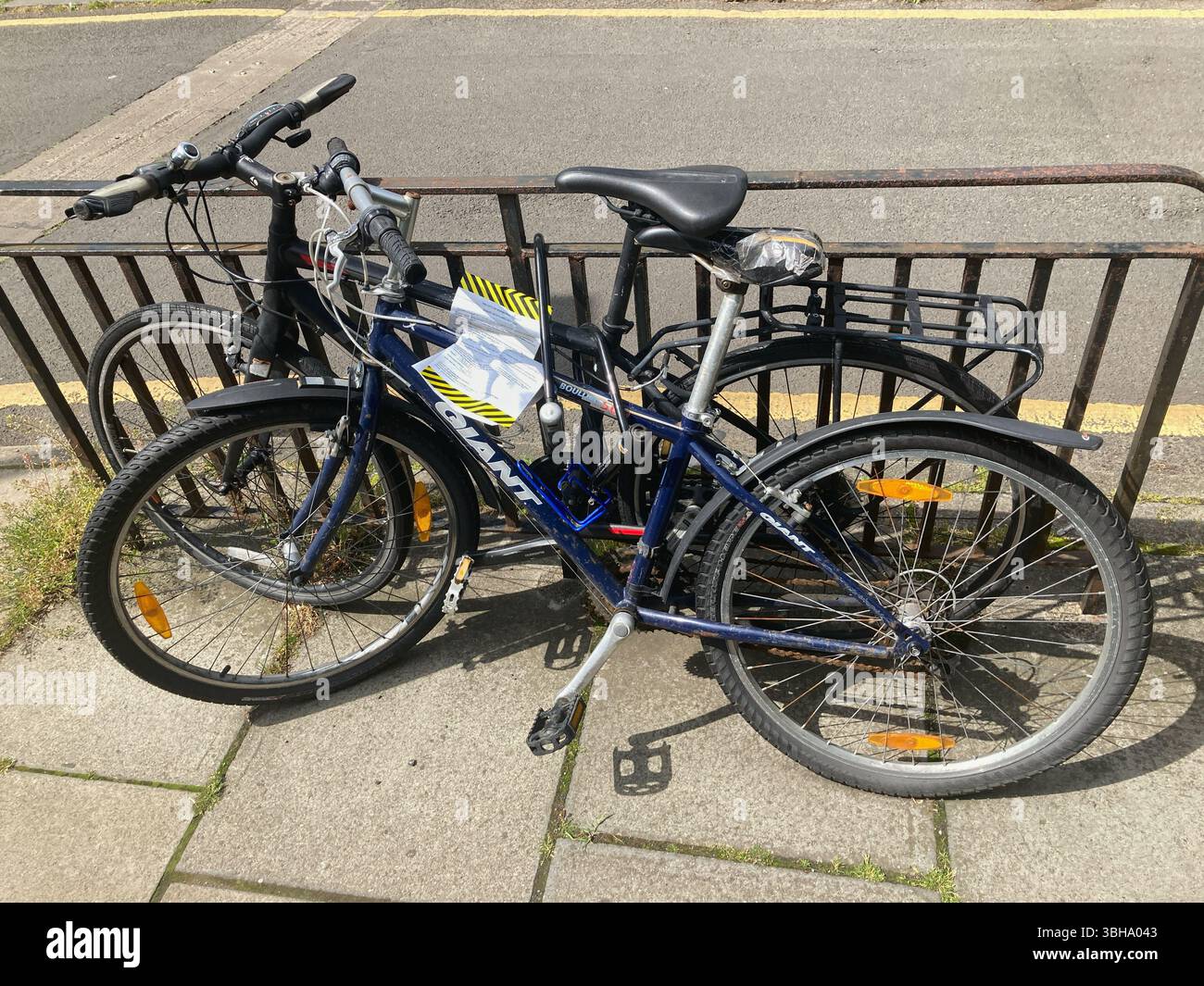 Two abandoned bicycles with an attached official council notice stating that the bikes will be removed in 7 days if they are not claimed by the owners - Smartphone Captured Stock Image