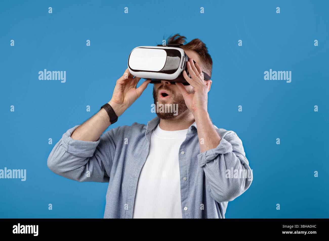Cool millennial guy experiencing virtual reality in VR headset on blue studio background Stock Photo