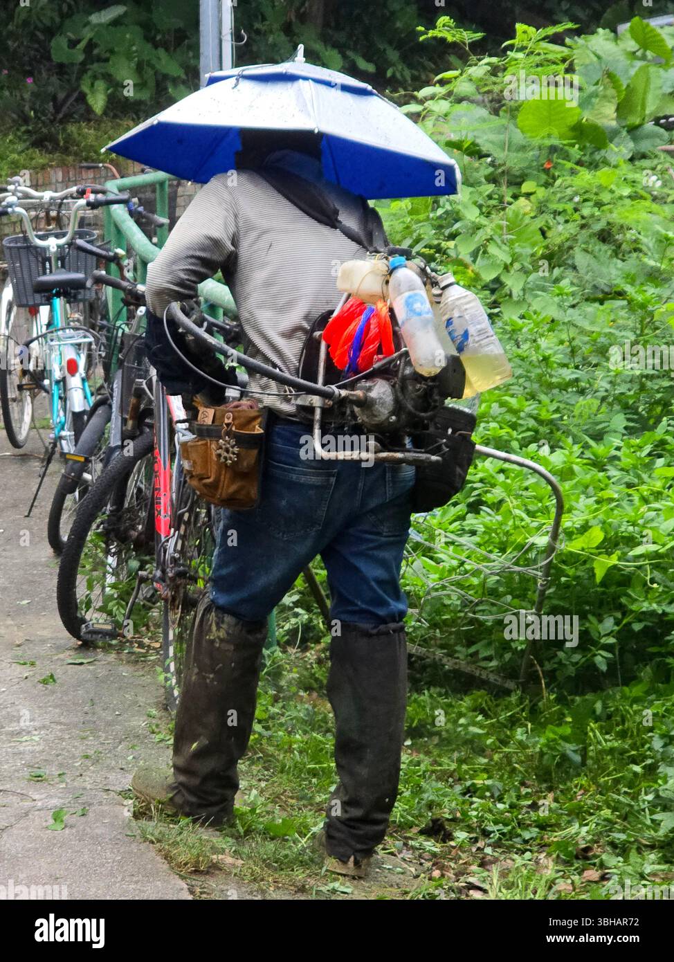 A man chopping down weeds and plants by the side of the trails on Lamma Island, Hong Kong. - Smartphone Captured Stock Image