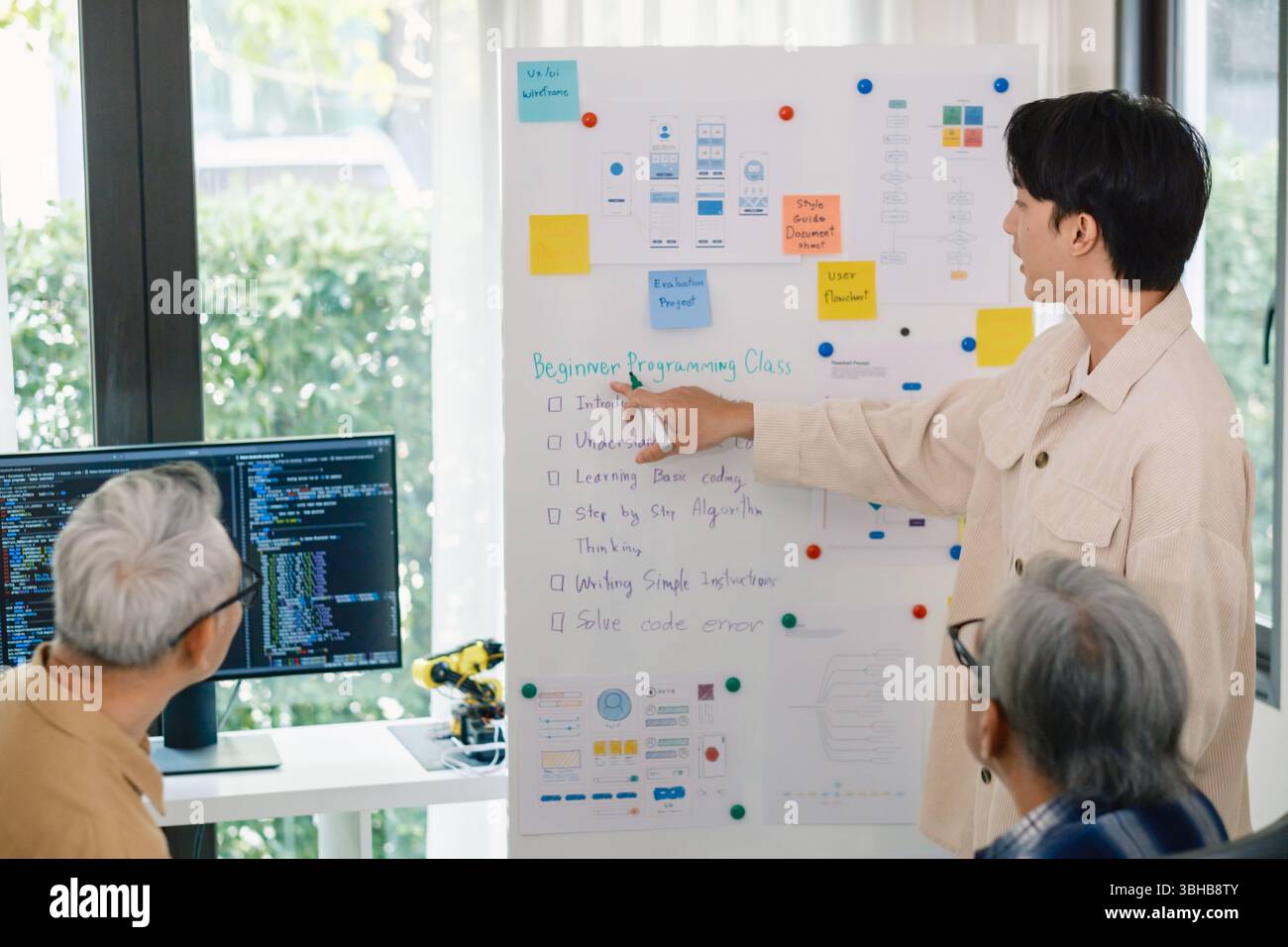 senior programmer bootcamlp,Asian young instructor guides senior learners through a programming on whiteboard, highlighting algorithm thinking and sim Stock Photo