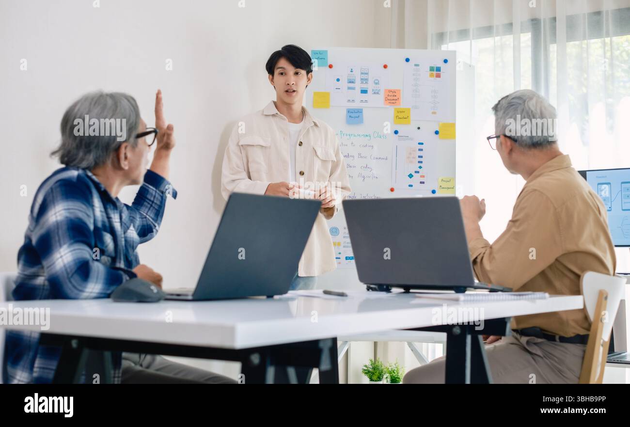 senior programmer bootcamlp,Asian young instructor guides senior learners through a programming on whiteboard, highlighting algorithm thinking and sim Stock Photo