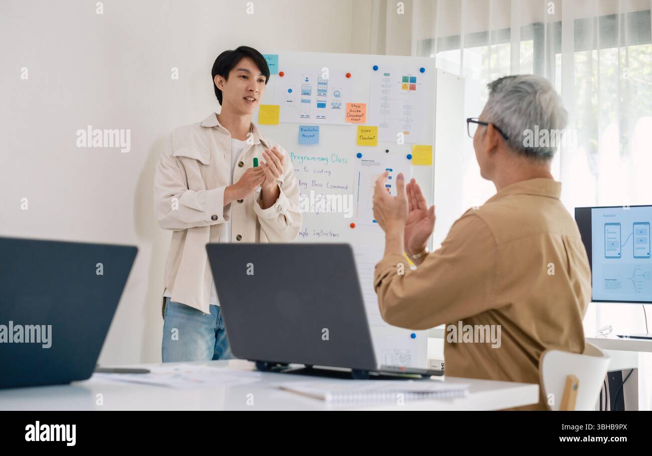 senior programmer bootcamlp,Asian young instructor guides senior learners through a programming on whiteboard, highlighting algorithm thinking and sim Stock Photo