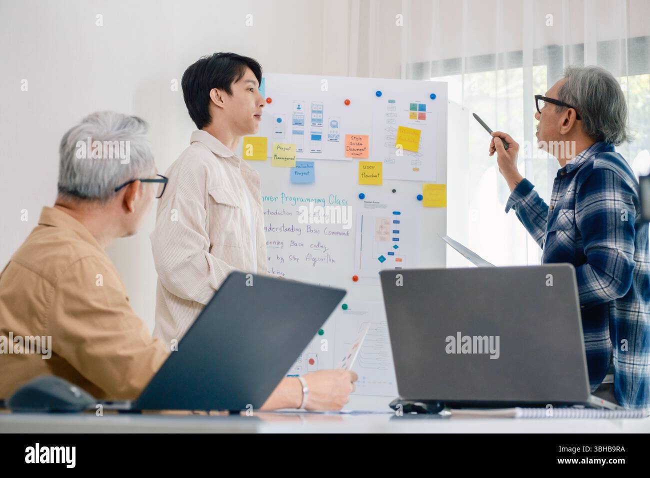 senior programmer bootcamlp,Asian young instructor guides senior learners through a programming on whiteboard, highlighting algorithm thinking and sim Stock Photo