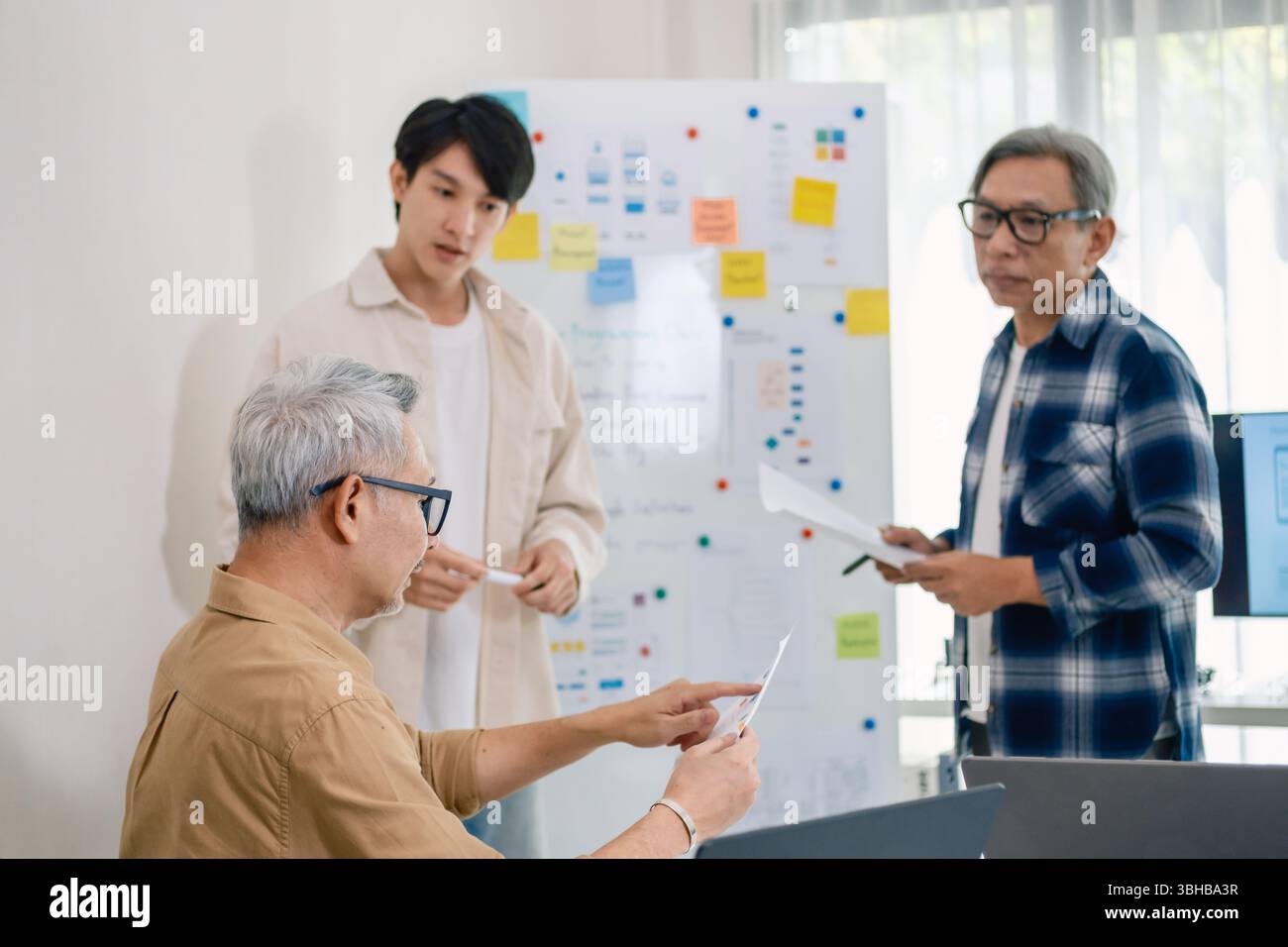 senior programmer bootcamlp,Asian young instructor guides senior learners through a programming on whiteboard, highlighting algorithm thinking and sim Stock Photo