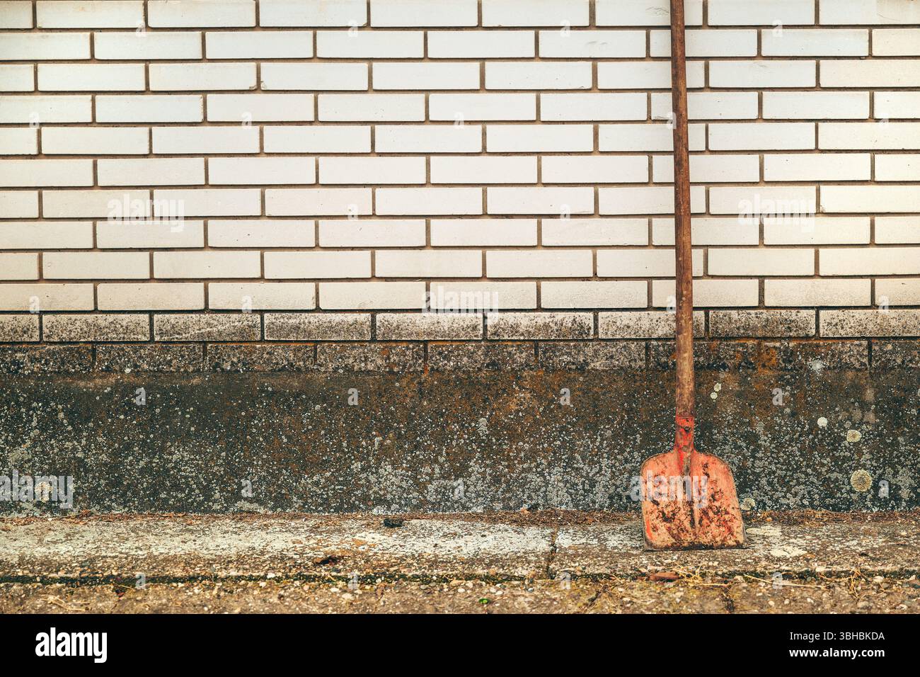 Old corroded shovel leaning on the white brick wall as copy space Stock Photo