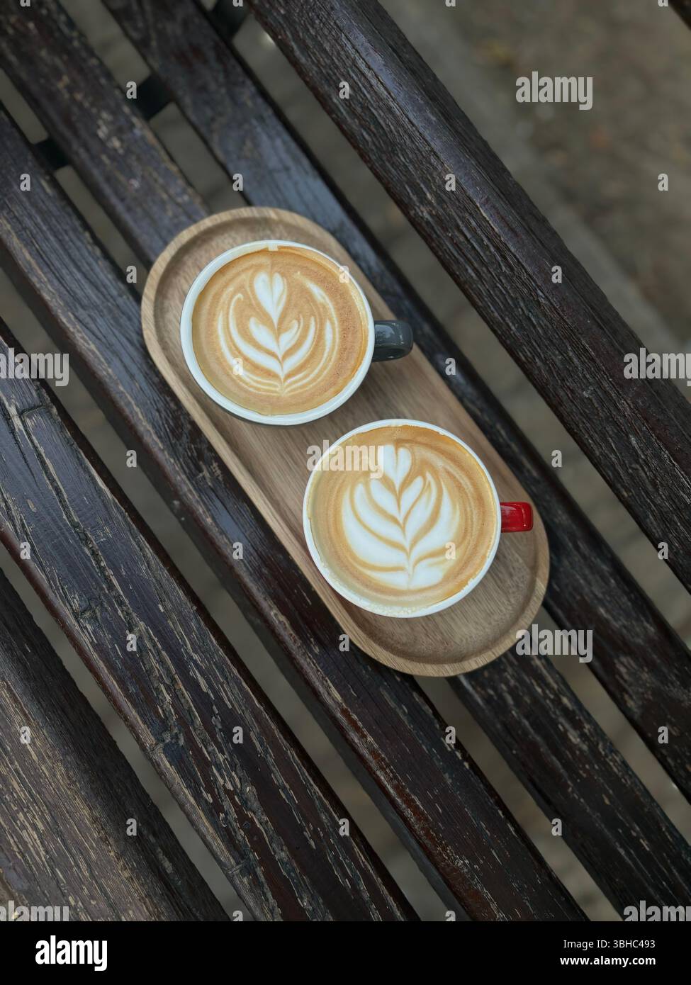 Two cappuccinos with latte art on a rustic wooden tray, served outdoors on a weathered bench. - Smartphone Captured Stock Image
