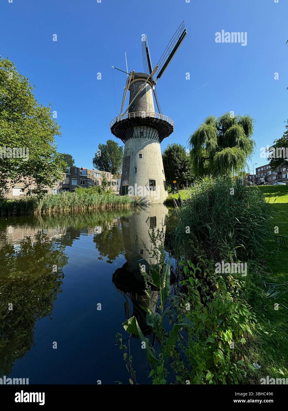 Traditional Dutch windmill reflecting in a calm canal on a sunny summer day in the Netherlands. - Smartphone Captured Stock Image