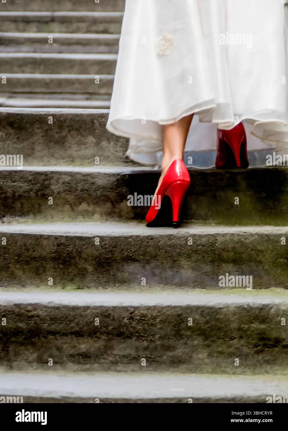 A woman in a long white dress and red high heels walks up a set of ...