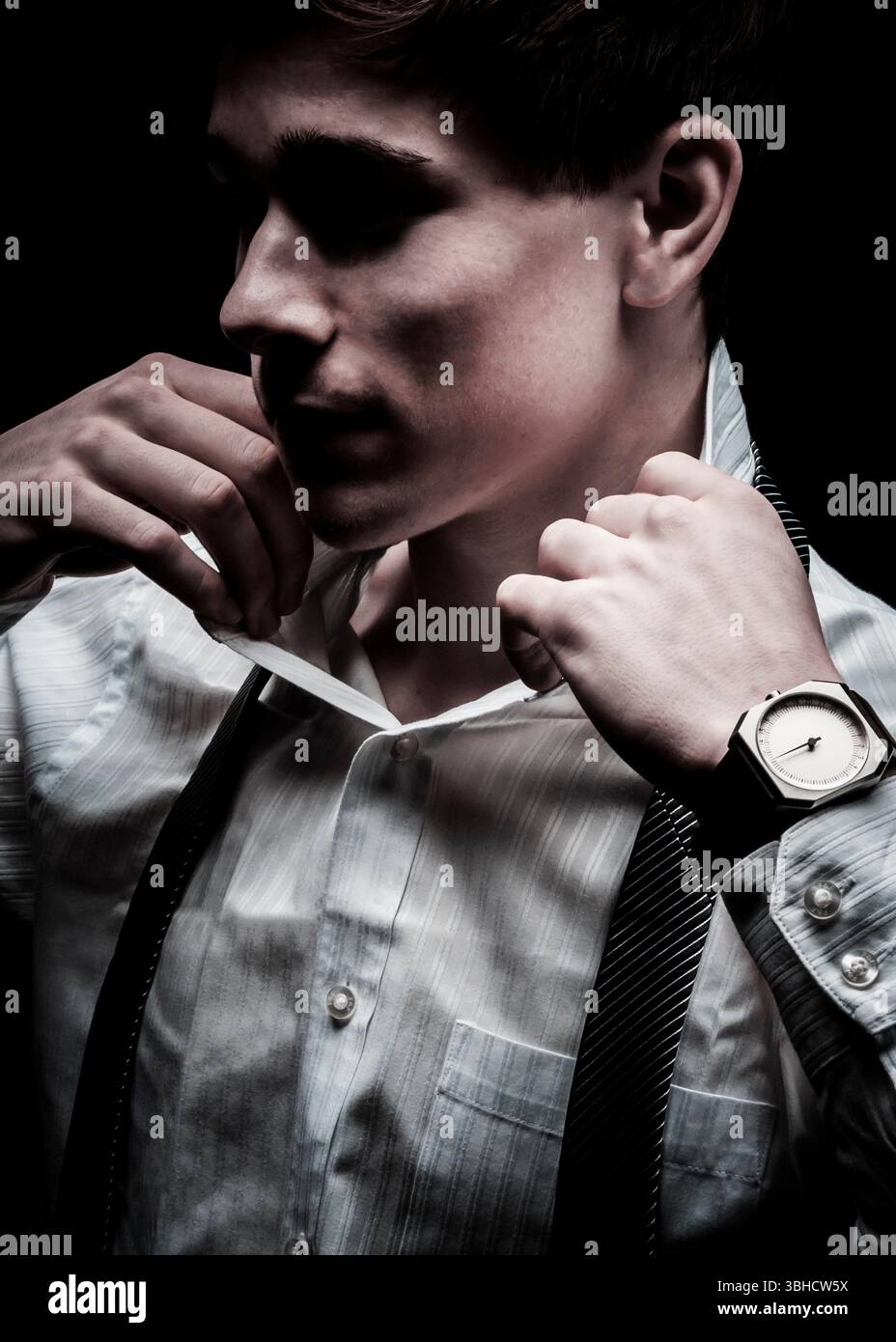 A young man adjusts his collar and tie in preparation for an event. The ...