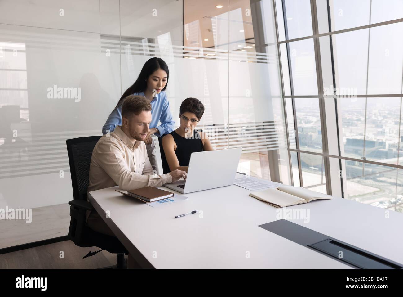 Three young multiracial colleagues working on joint task using laptop Stock Photo