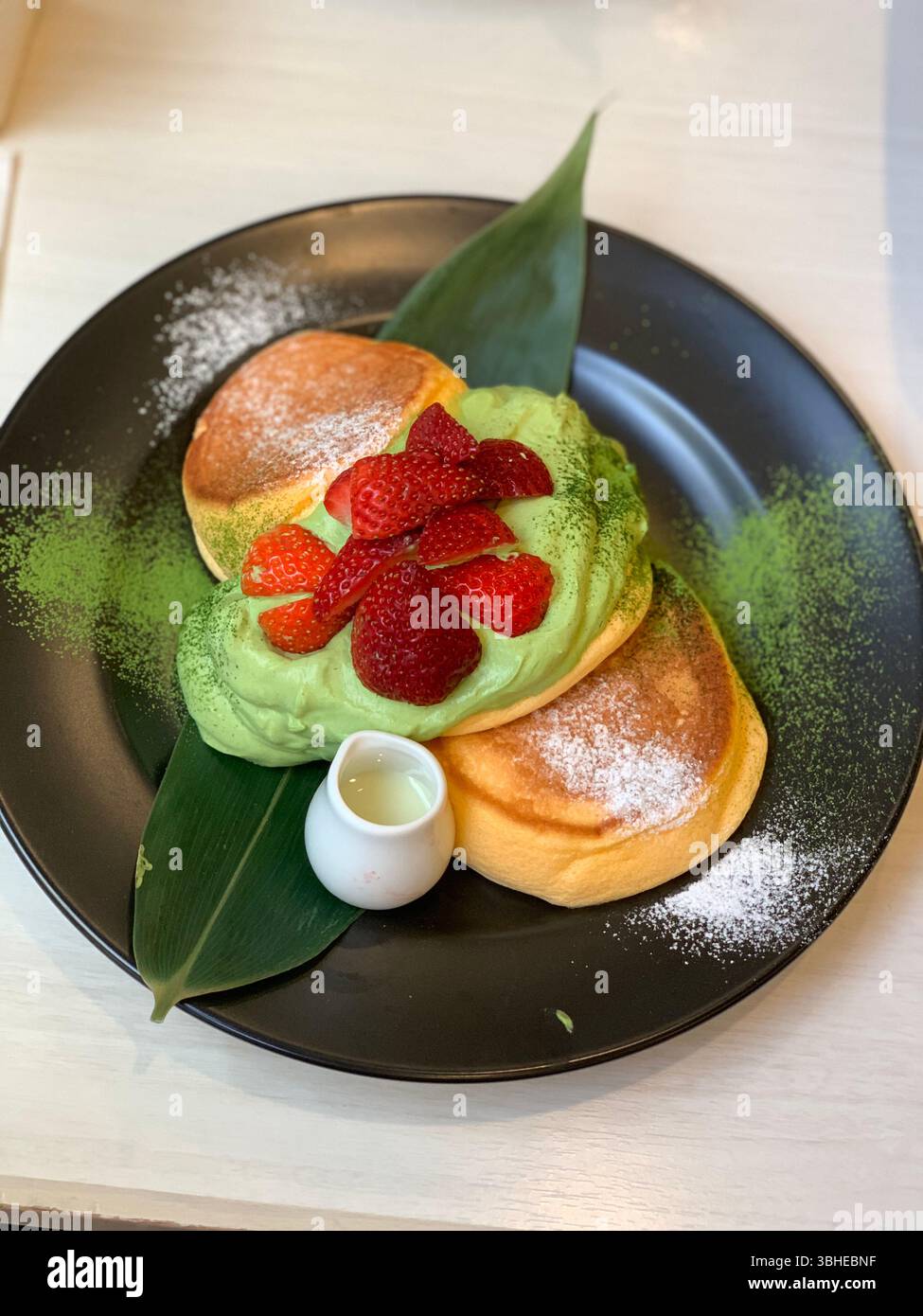 A stack of airy Japanese fluffy pancakes topped with silky matcha cream and strawberries - Smartphone Captured Stock Image
