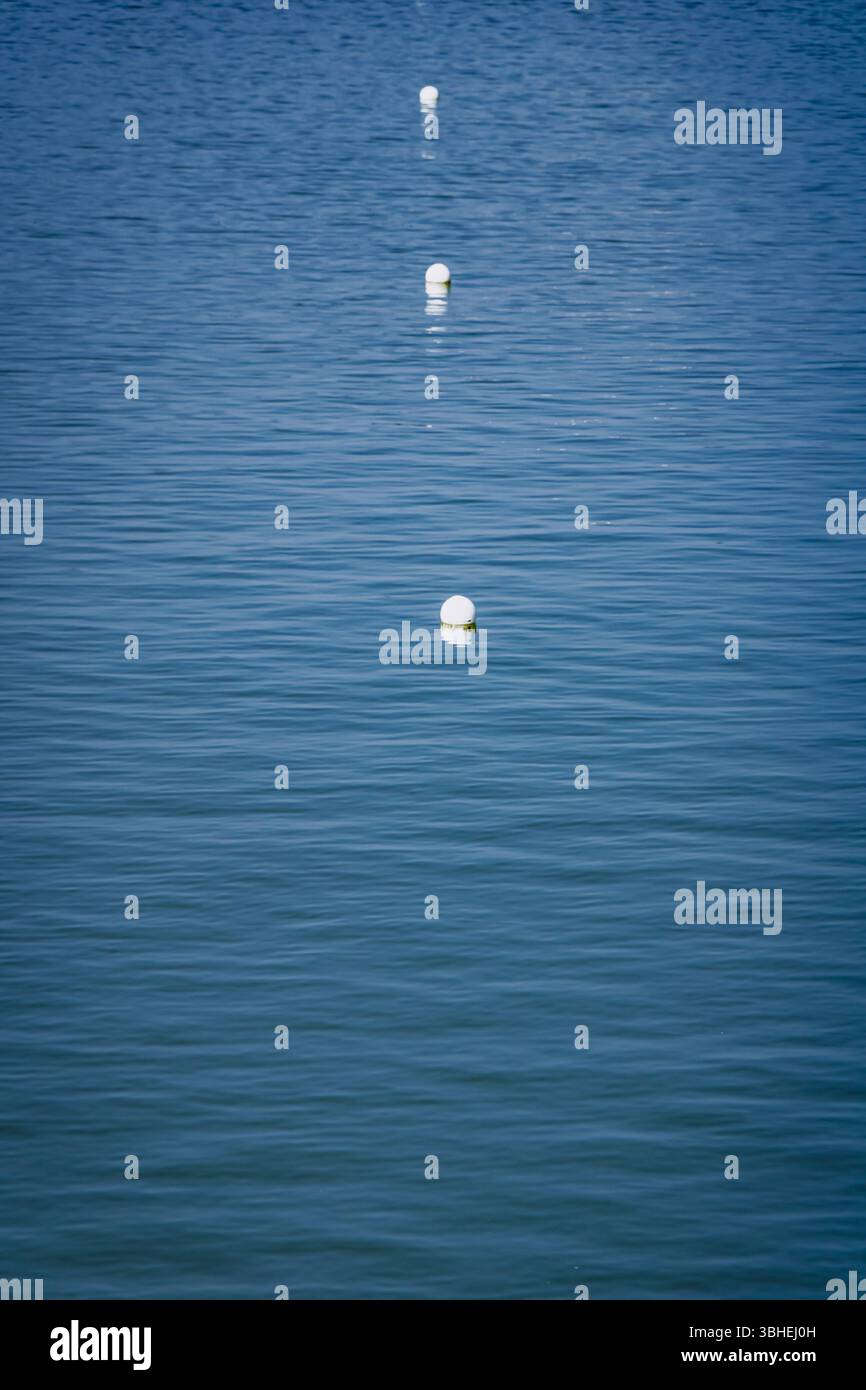 Buoys drift peacefully in a tranquil lake, reflecting sunlight against the bright blue water. Gentle waves create a soft ripple, enhancing the serene Stock Photo