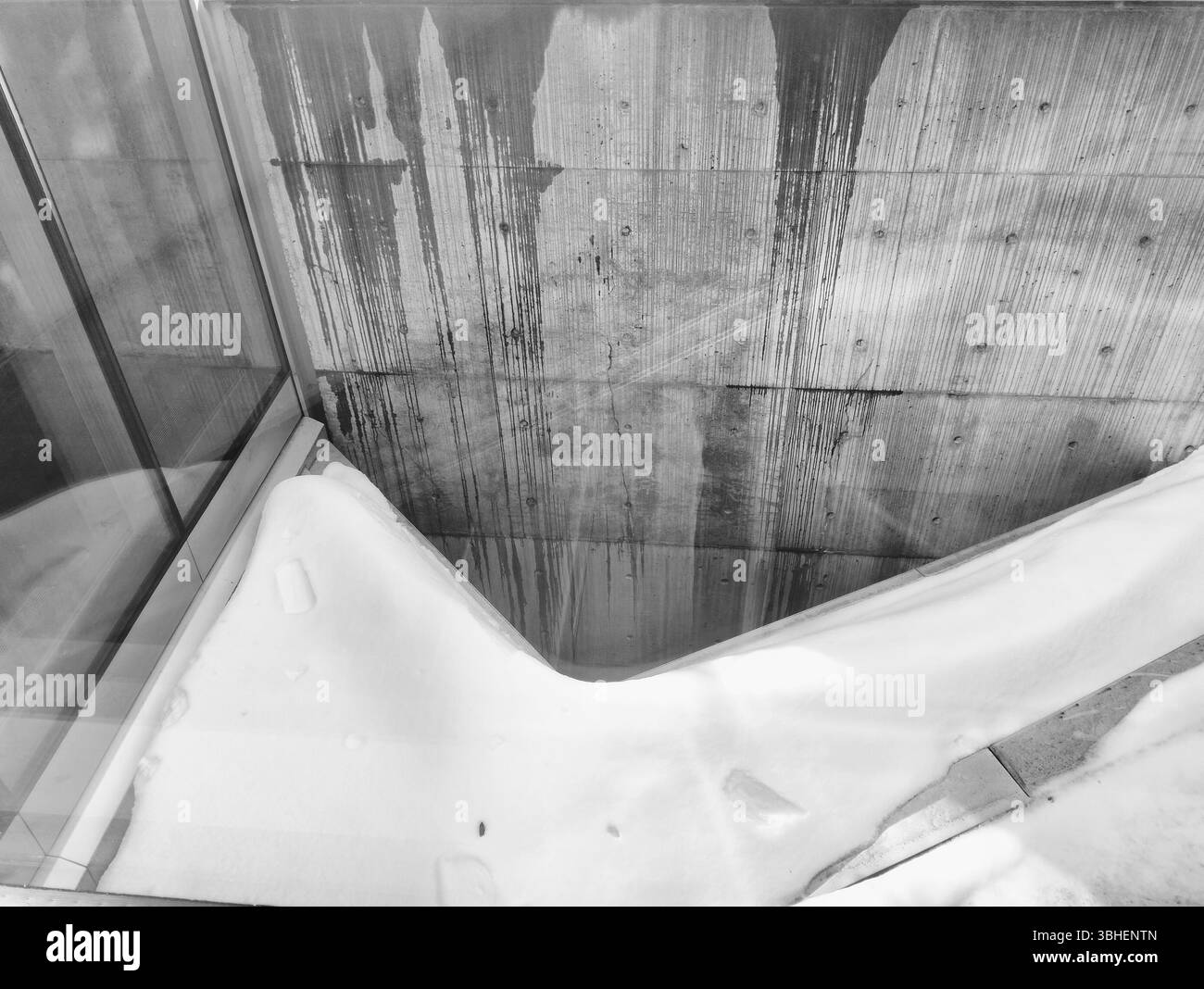 A black and white photograph captures an abstract architectural scene. A concrete wall with vertical stains serves as a backdrop. - Smartphone Captured Stock Image