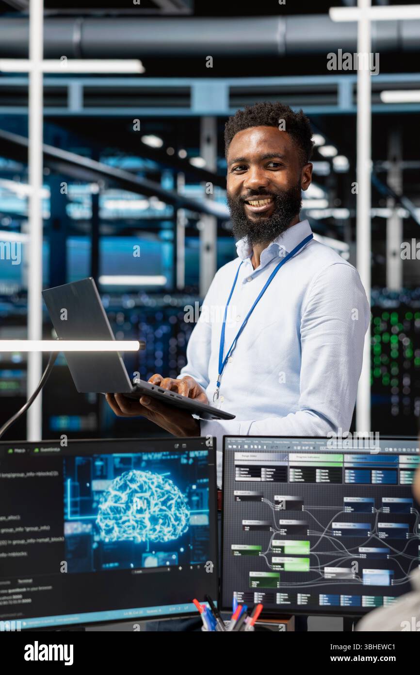 Cheerful man in server hub facility using artificial intelligence to perform demanding computing tasks. Jolly admin in data center uses AI technology for machine learning workloads Stock Photo