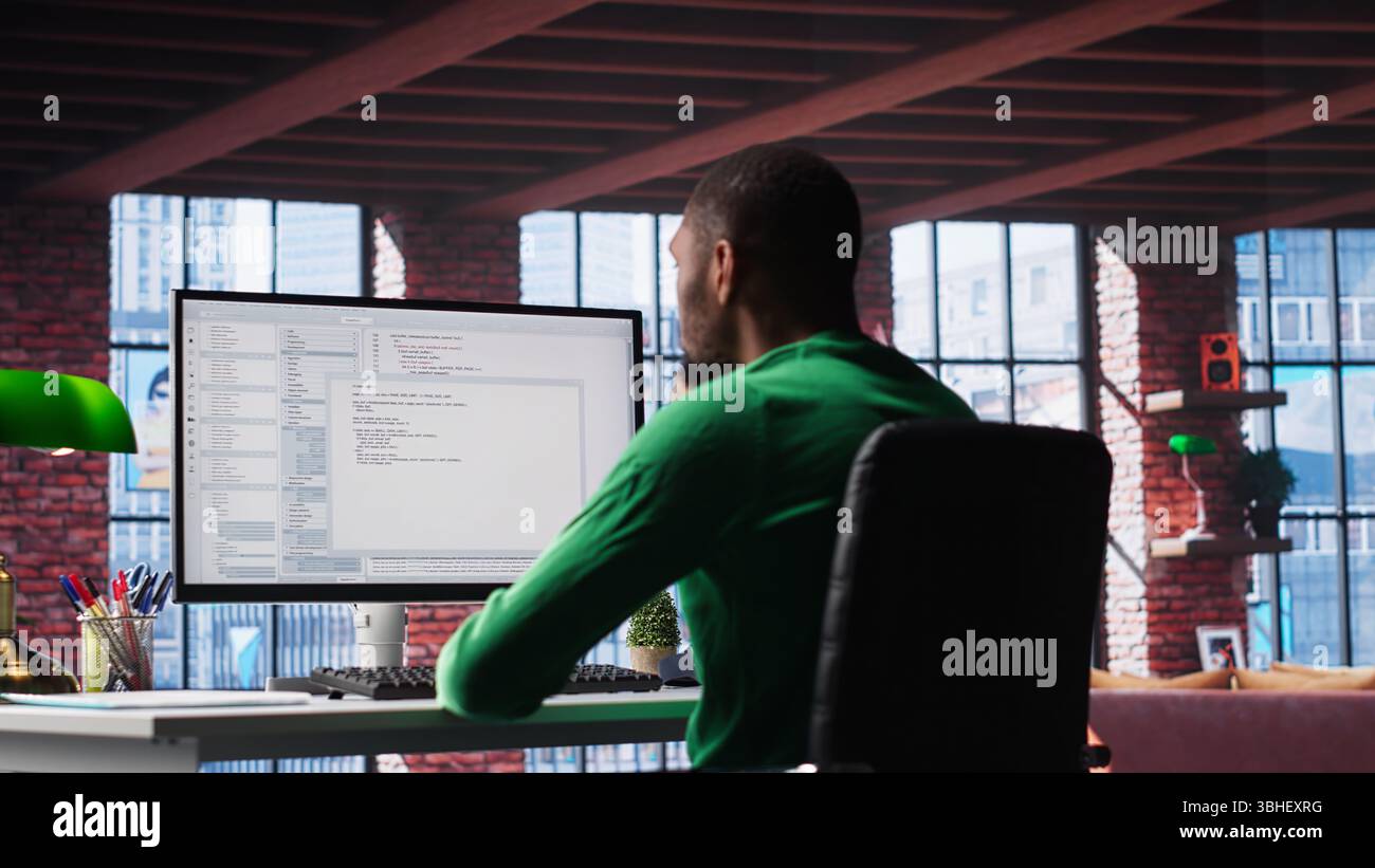 Black IT developer at PC coding and creating an app software, implementing algorithms to fix errors. Engineer in his loft working with code language, optimizing app performance. Camera B. Stock Photo