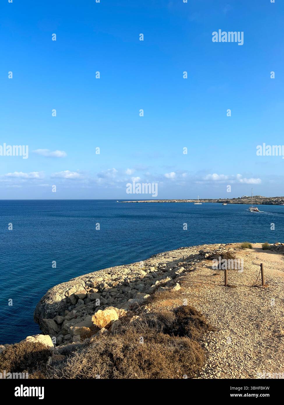 Peaceful rocky coastline with deep blue sea and boats in the distance under a clear sky. Ideal for themes of travel, exploration, and natural beauty. - Smartphone Captured Stock Image