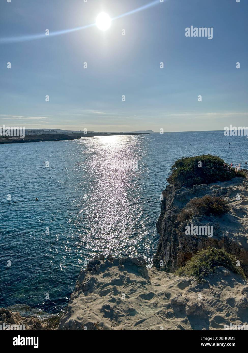 Golden sun reflecting over the tranquil sea, with rugged cliffs in the foreground. Perfect for themes of nature, solitude, and coastal landscapes. - Smartphone Captured Stock Image