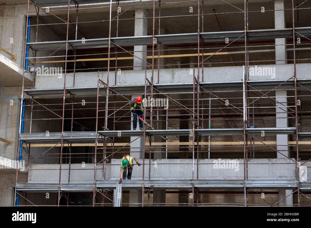 Two male workers assembling scaffolding on a construction site in an urban area during daylight hours Stock Photo