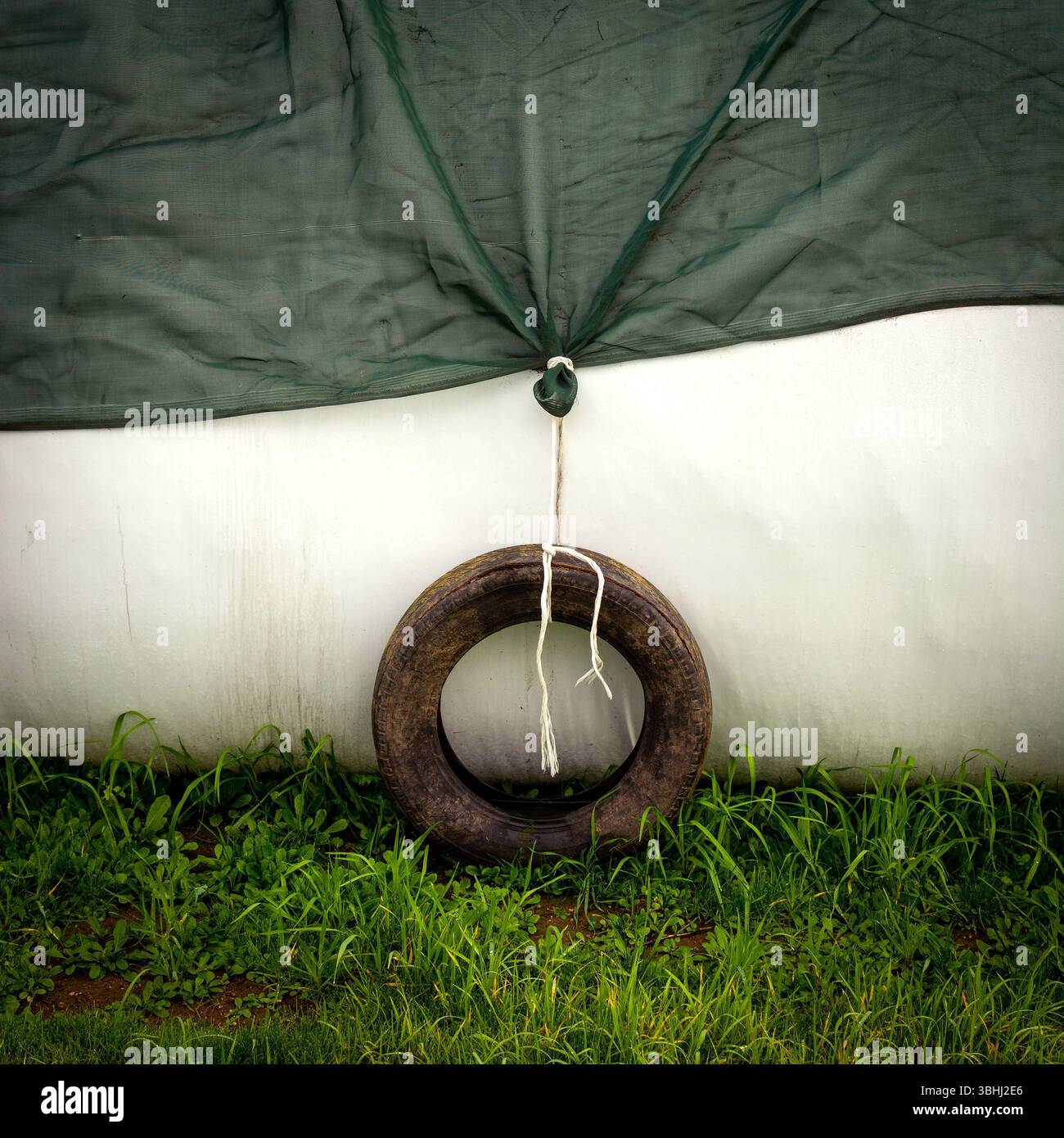 A weathered tire is tied to a green tarp, providing stability in a subtle, serene outdoor setting. Auvergne. France Stock Photo