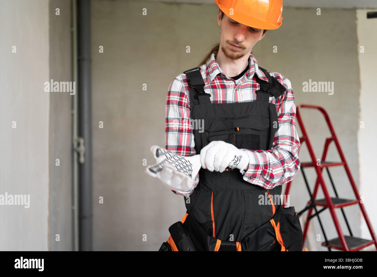 Construction worker or young builder putting gloves before work standing in house for renovation Stock Photo