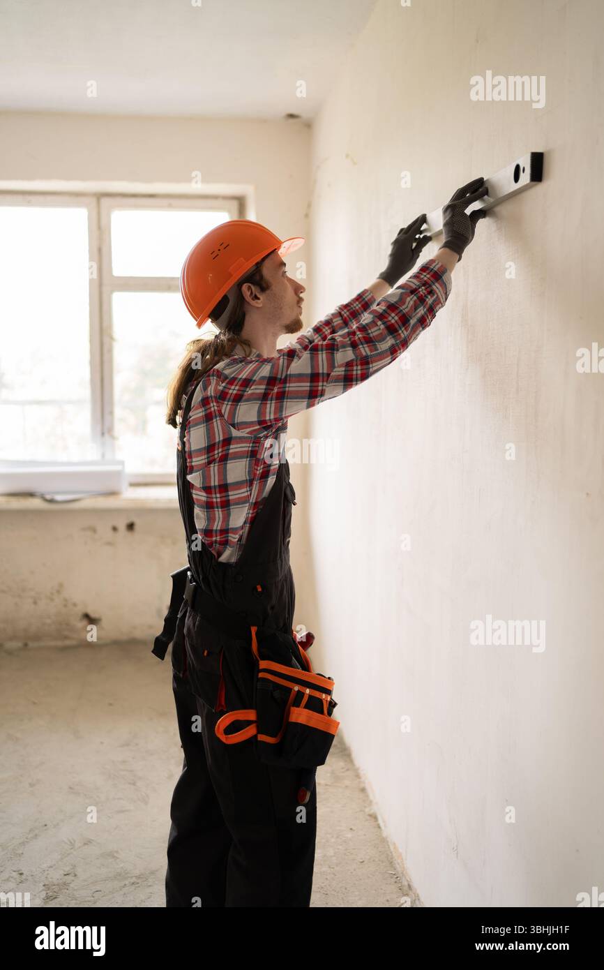 Builder wearing protective helmet uses a spirit level making renovation ...