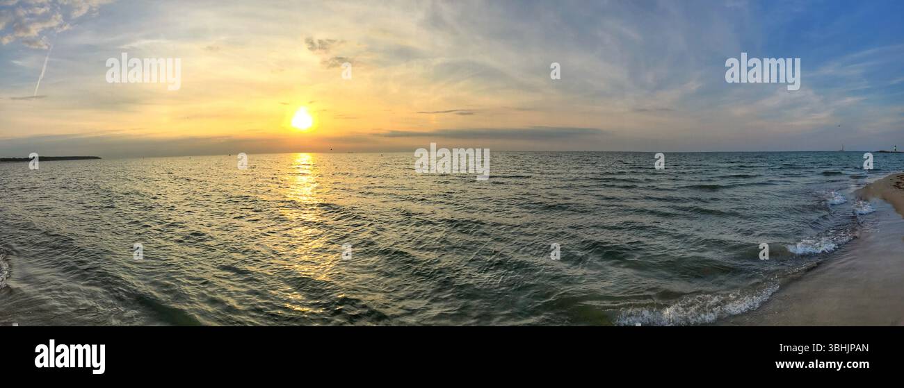 A beautiful panoramic coastal view showcasing a serene sunset over calm ocean waves. The warm hues of the sunset create a tranquil atmosphere, enhance Stock Photo