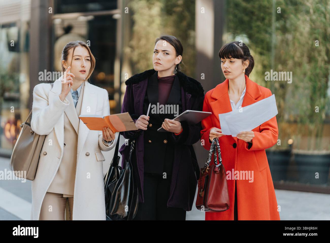 Three female professionals discuss work outdoors holding documents and tablets Stock Photo