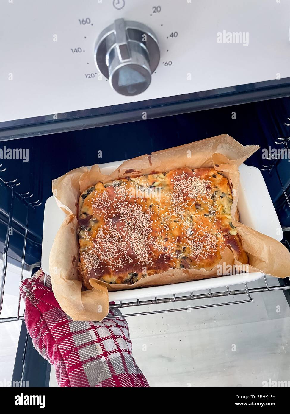 Top view of hand in oven mitt taking freshly baked pie in ceramic form from oven Stock Photo