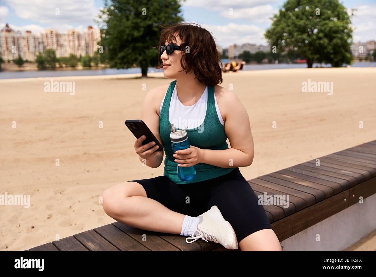 A pretty young woman relaxes by the water, holding a drink while ...