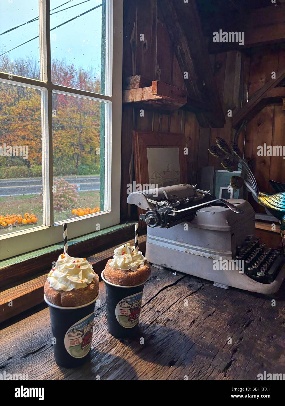 Two coffees topped with donuts and whipped cream overlooking an Autumn day - Smartphone Captured Stock Image