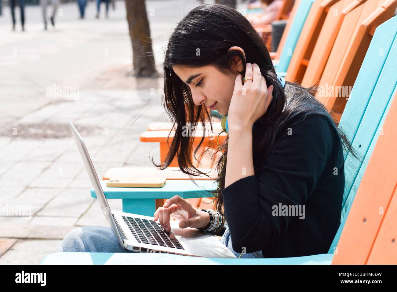 Young woman sitting on city street using laptop computer Stock Photo
